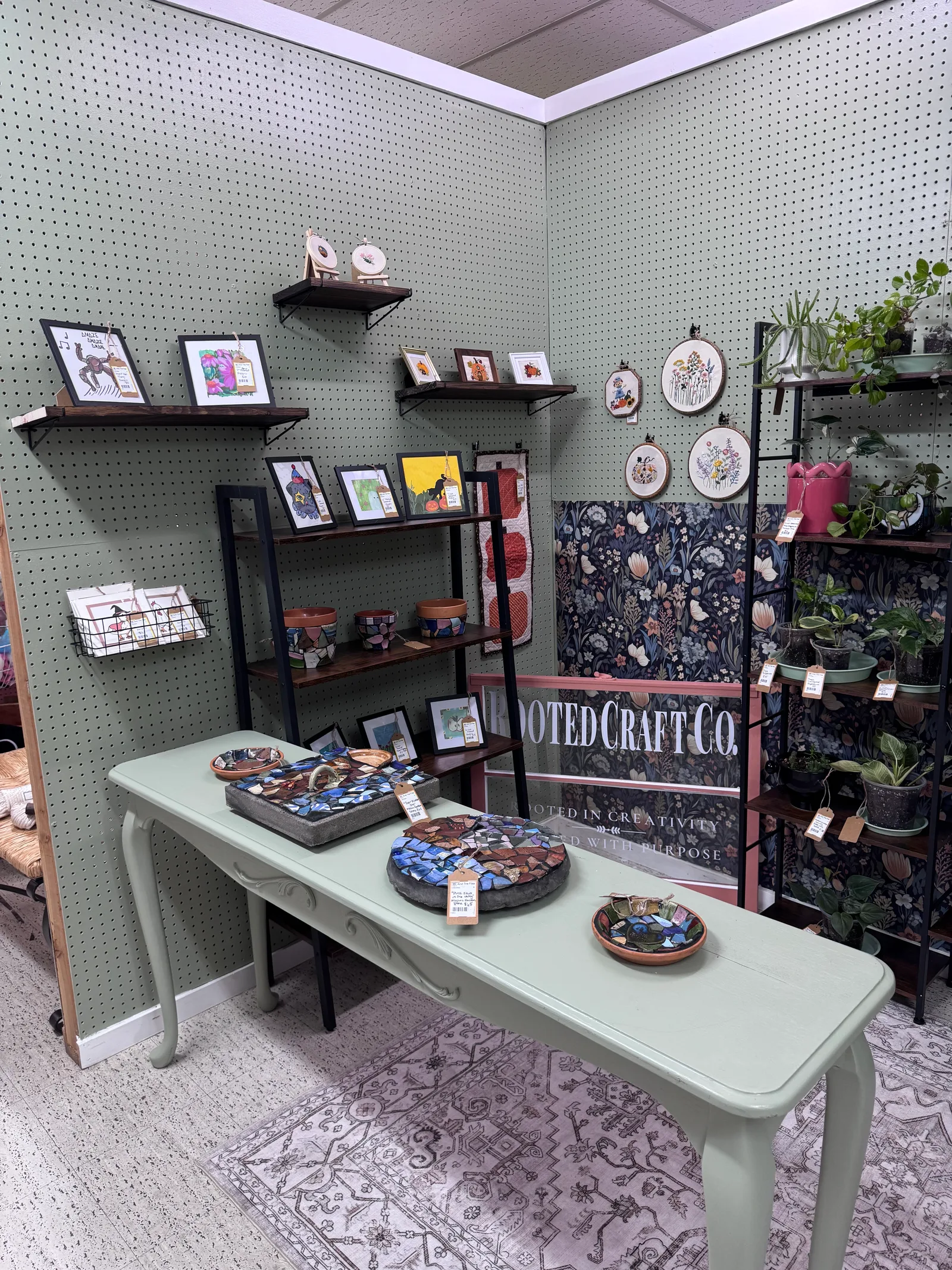 Rooted Craft Co booth with mosaic art, framed drawings, embroidery, and plants